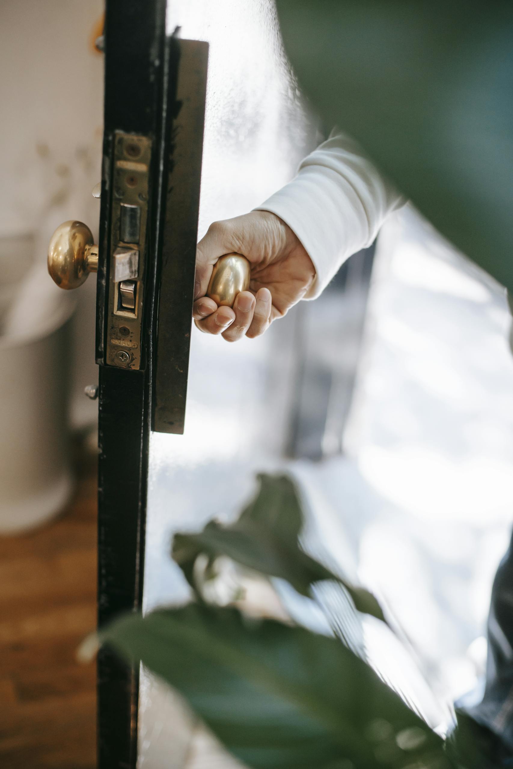 Close-up of a hand opening a door with a brass handle leading to a bright interior.
